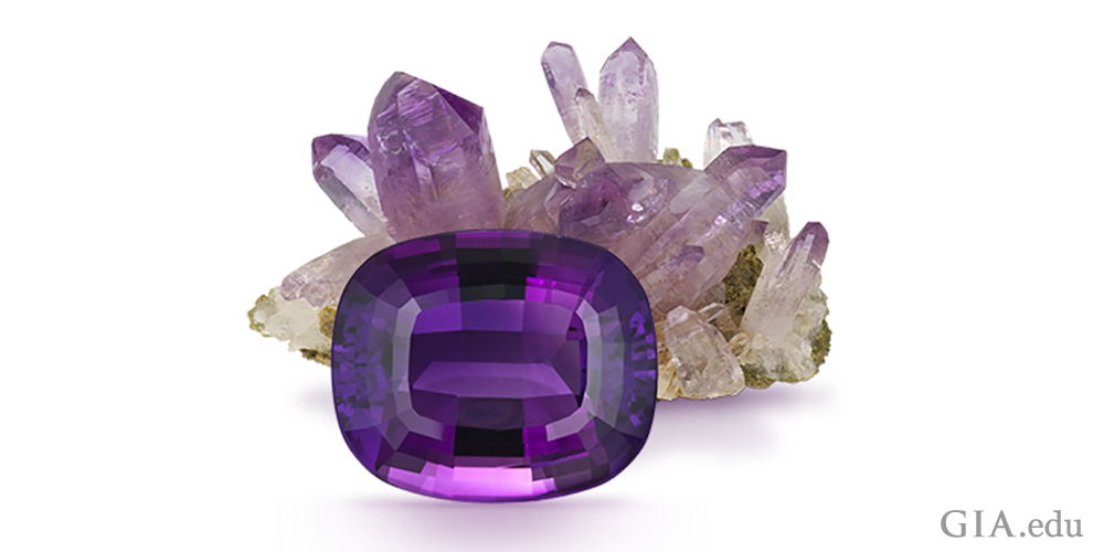 A 22.62 carat (ct) cushion cut amethyst is the dramatic foreground to the amethyst rough behind it.