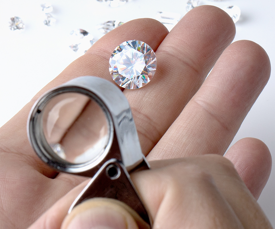 A hand holding a diamond with a loupe